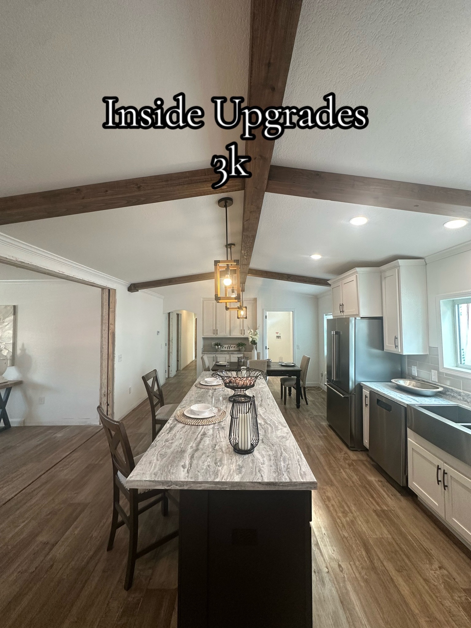 Modern kitchen with marble island, wooden beams, and elegant pendant lights. Stainless steel appliances add a sleek touch, conveying a warm, upgraded feel. Text reads "Inside Upgrades 3k."
