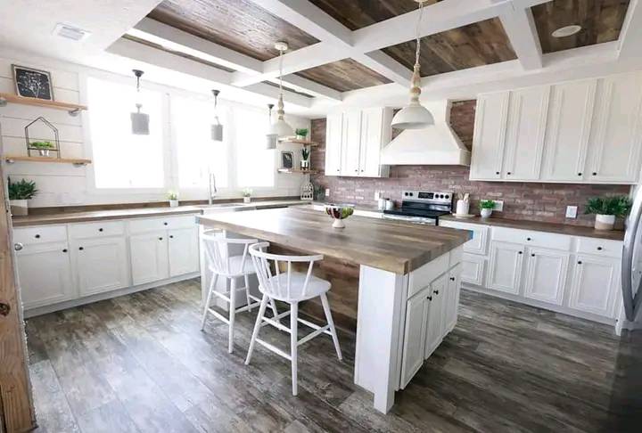 Spacious modern kitchen with white cabinets, wooden countertops, and island. Brick backsplash, pendant lights, and plants create a cozy, inviting atmosphere.