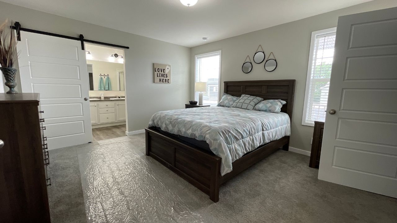 Spacious bedroom with a neatly made bed, soft lighting, and cozy ambiance. Decorative wall art and a sliding barn door leading to a modern bathroom.