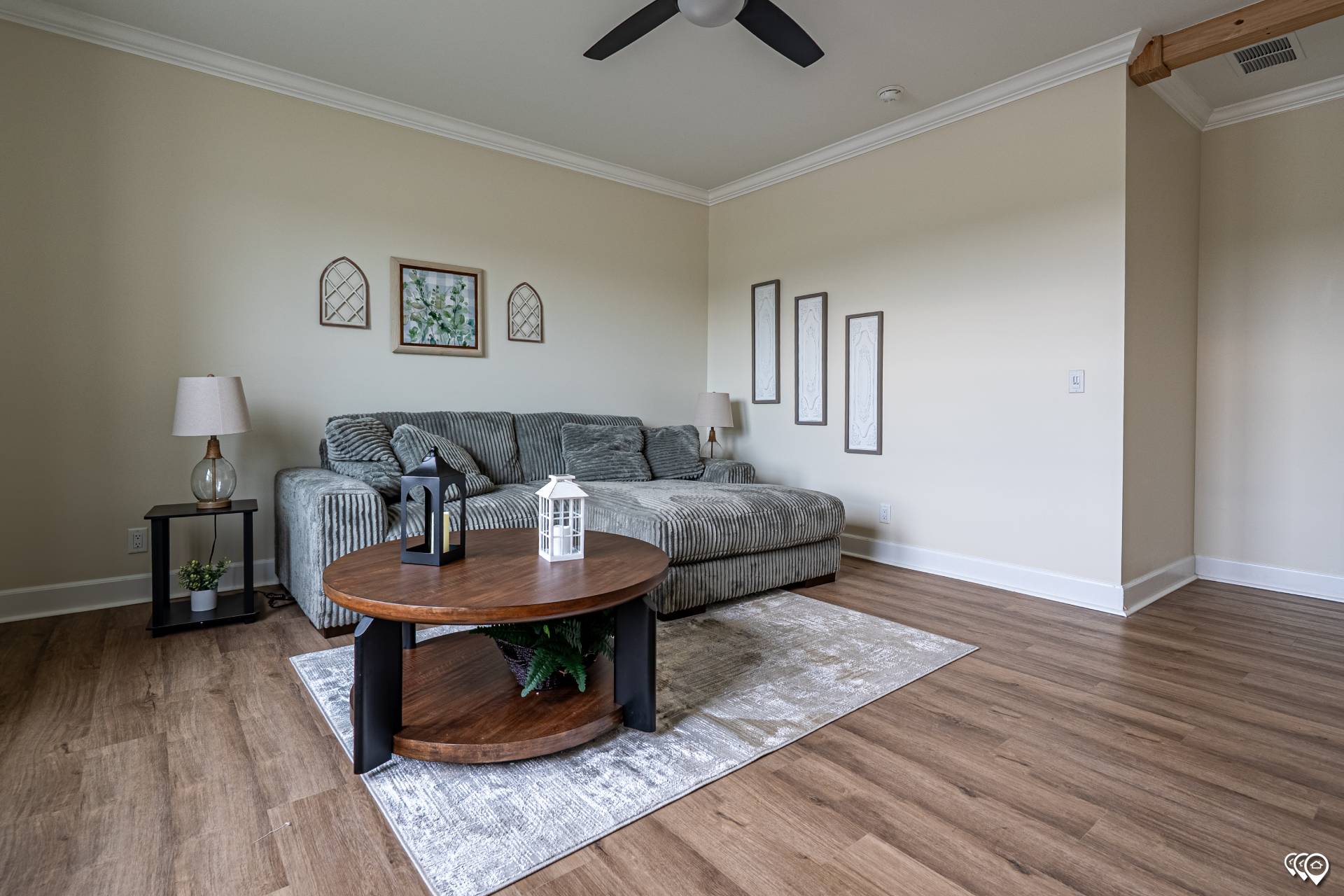 Modern living room with a striped gray sectional sofa, wooden coffee table with lanterns, wall art, and a ceiling fan. Warm and inviting ambiance.