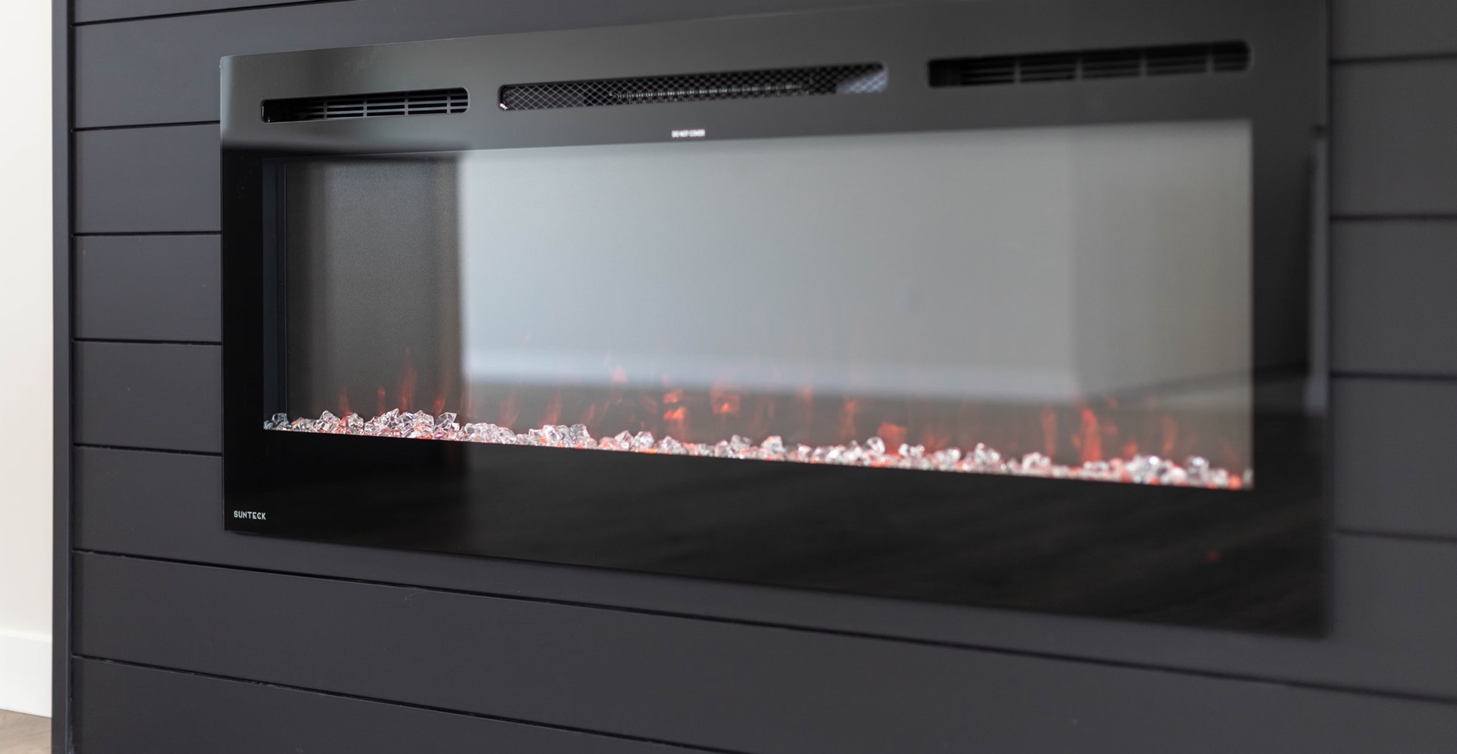 Modern electric fireplace with glowing red flames and decorative clear crystals inside a sleek, black frame. It conveys warmth and contemporary style.