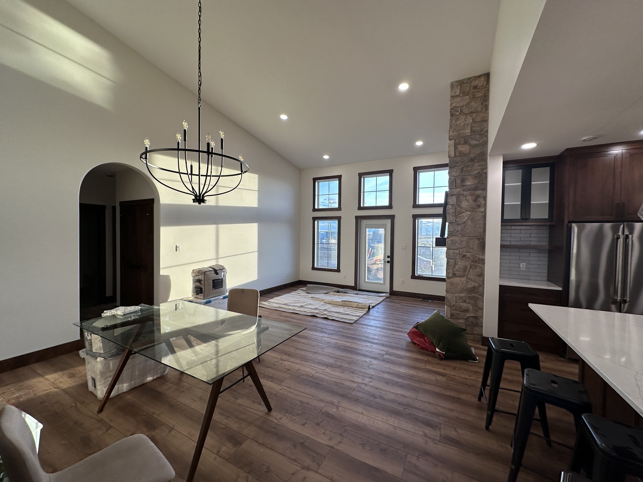 A modern living area with high ceilings and natural light. Features a glass dining table, stone fireplace, and large windows. Warm and inviting atmosphere.