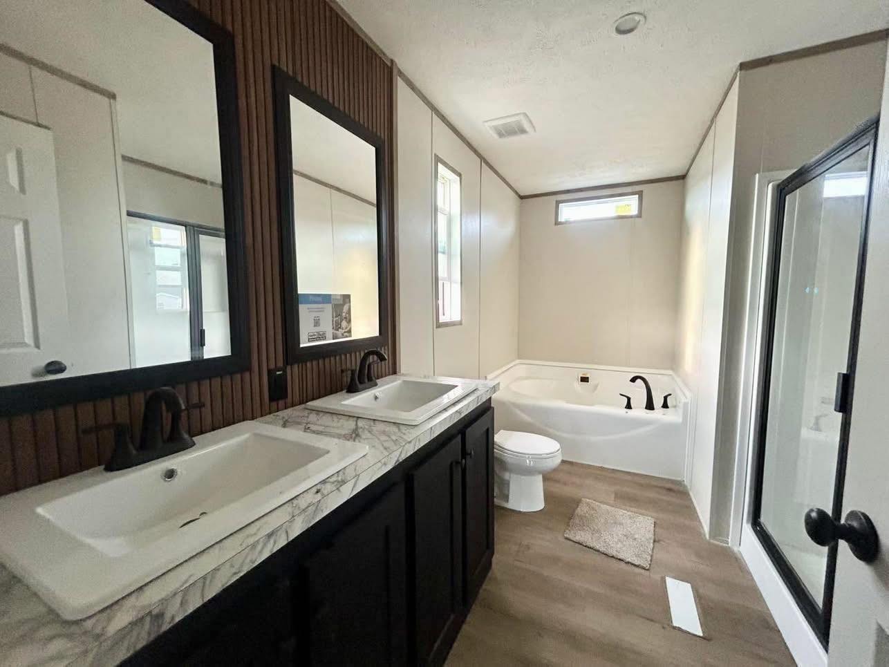 Modern bathroom with two sinks on a marble countertop, dark wood cabinets, a freestanding bathtub, shower with glass door, and neutral tones.
