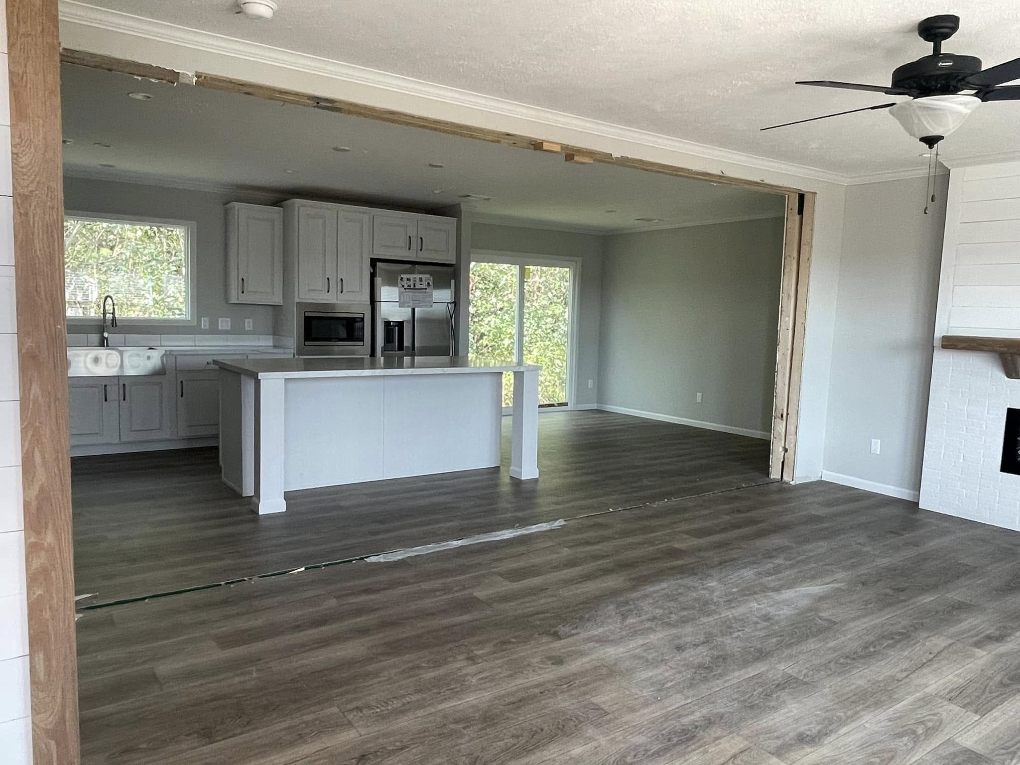 Open-concept living area with gray kitchen cabinets, stainless steel appliances, and a large island. Wooden floors and ceiling fan add warmth.