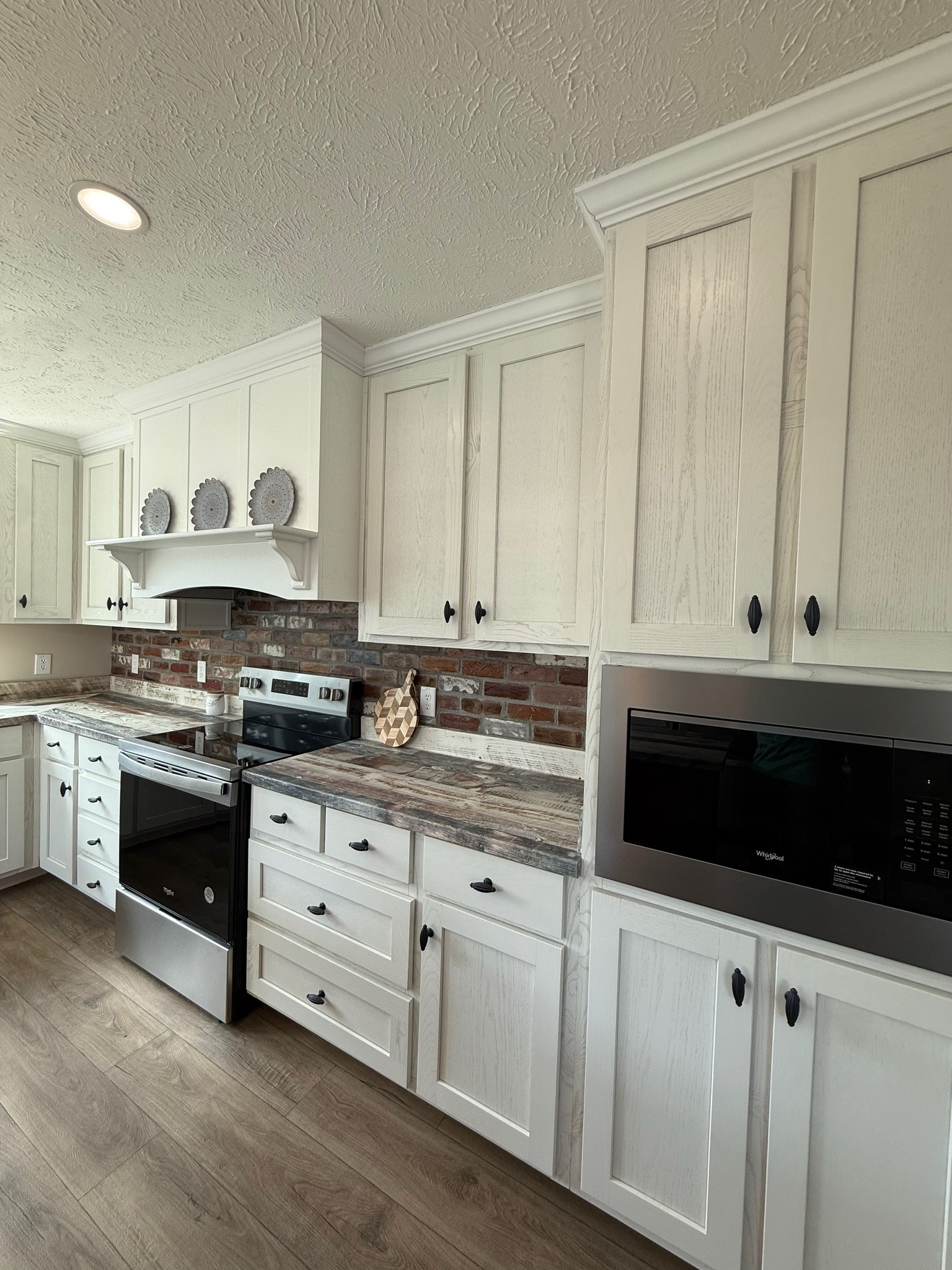 Bright kitchen with off-white cabinets, stainless steel oven and microwave, brick backsplash, decorative plates, and wood-style flooring. Cozy and modern.