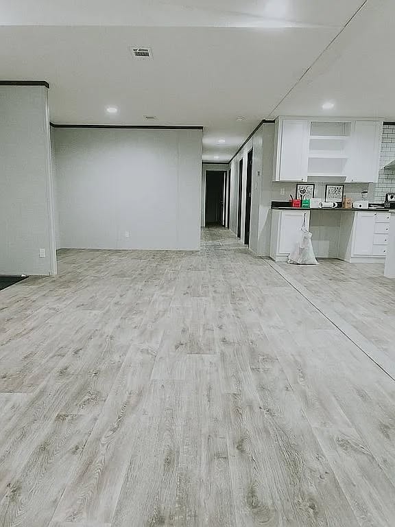 Spacious, modern room with light wood laminate flooring. White walls and cabinets with a black countertop. Bright, minimalist aesthetic.