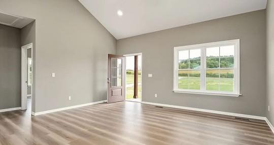 Spacious, empty room with light wood floors and pale gray walls. A large window and open door reveal a lush green landscape, conveying tranquility.