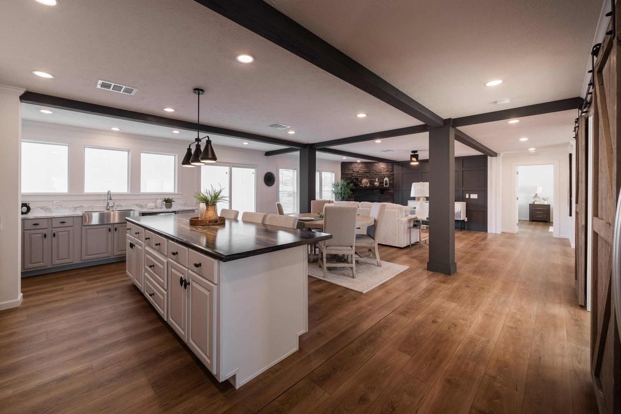 Spacious open-concept kitchen and living area with wooden floors. Features a large island, white cabinets, cozy seating, and natural light through windows.