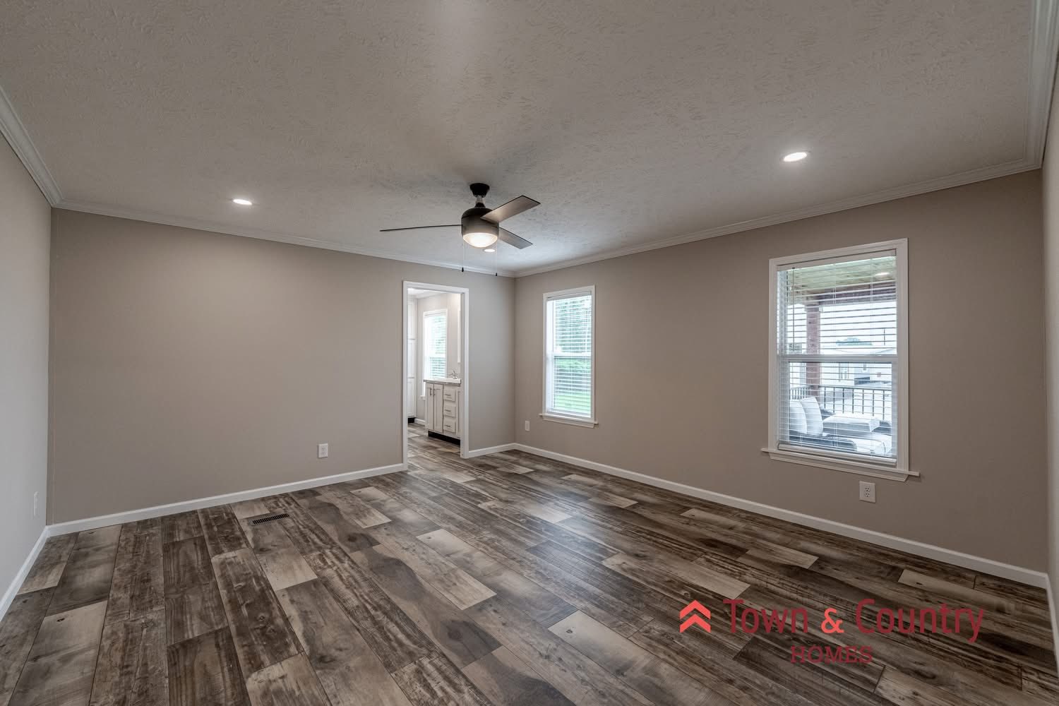 A spacious, neutral-toned room with wooden flooring, ceiling fan, and two windows letting in natural light. Minimalist and serene atmosphere.