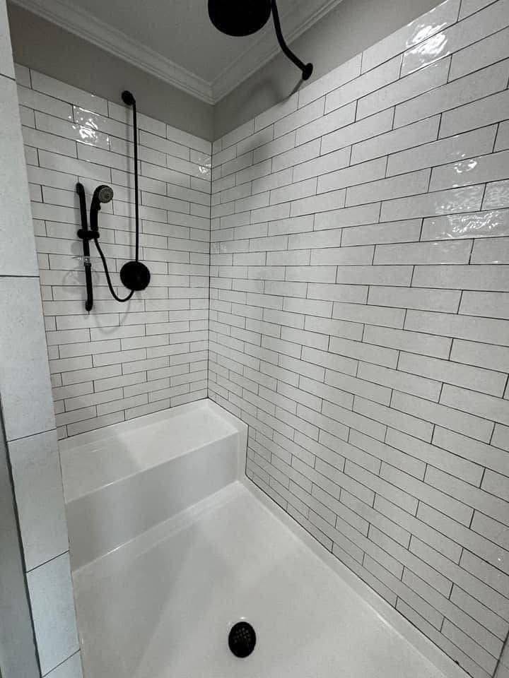 Modern bathroom shower with white subway tiles, black fixtures, and a built-in bench. The space is clean and minimalist, evoking a sleek, modern vibe.