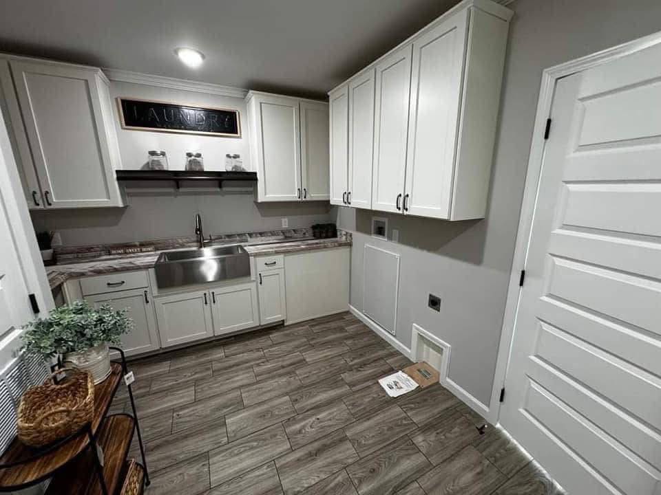 A modern laundry room with white cabinets, a stainless steel sink, and wooden flooring. A small door at the bottom right adds a playful touch.