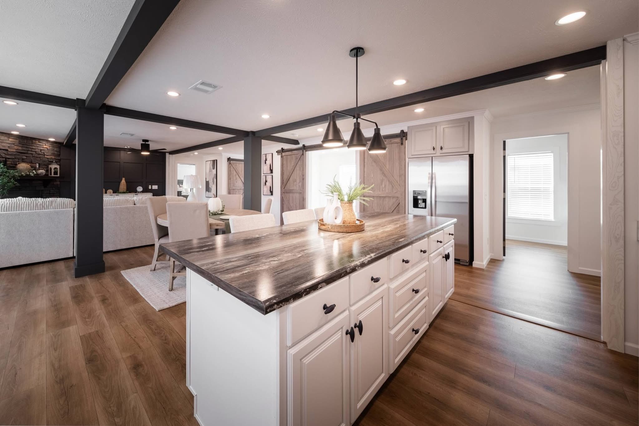 Modern open-concept kitchen featuring a large island with dark marble countertop, white cabinetry, pendant lights, and a warm, inviting atmosphere.