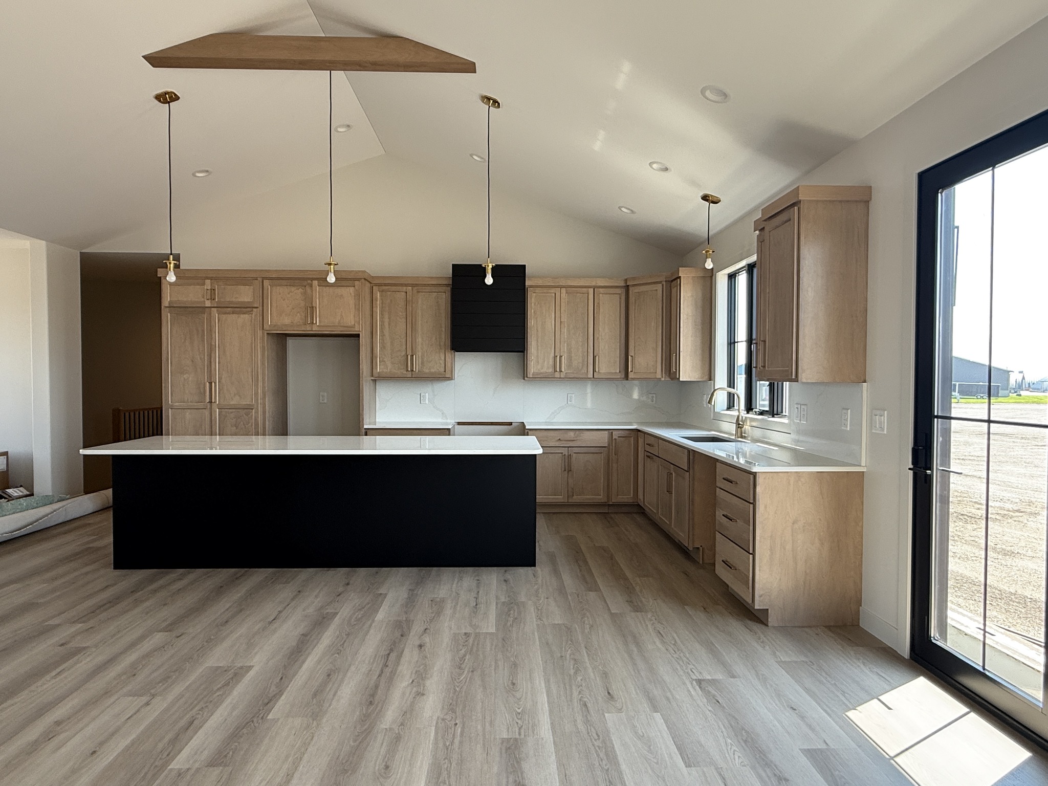 Modern kitchen with light wood cabinets, an L-shaped counter, and a large island. Pendant lights hang from a vaulted ceiling, creating an airy feel.