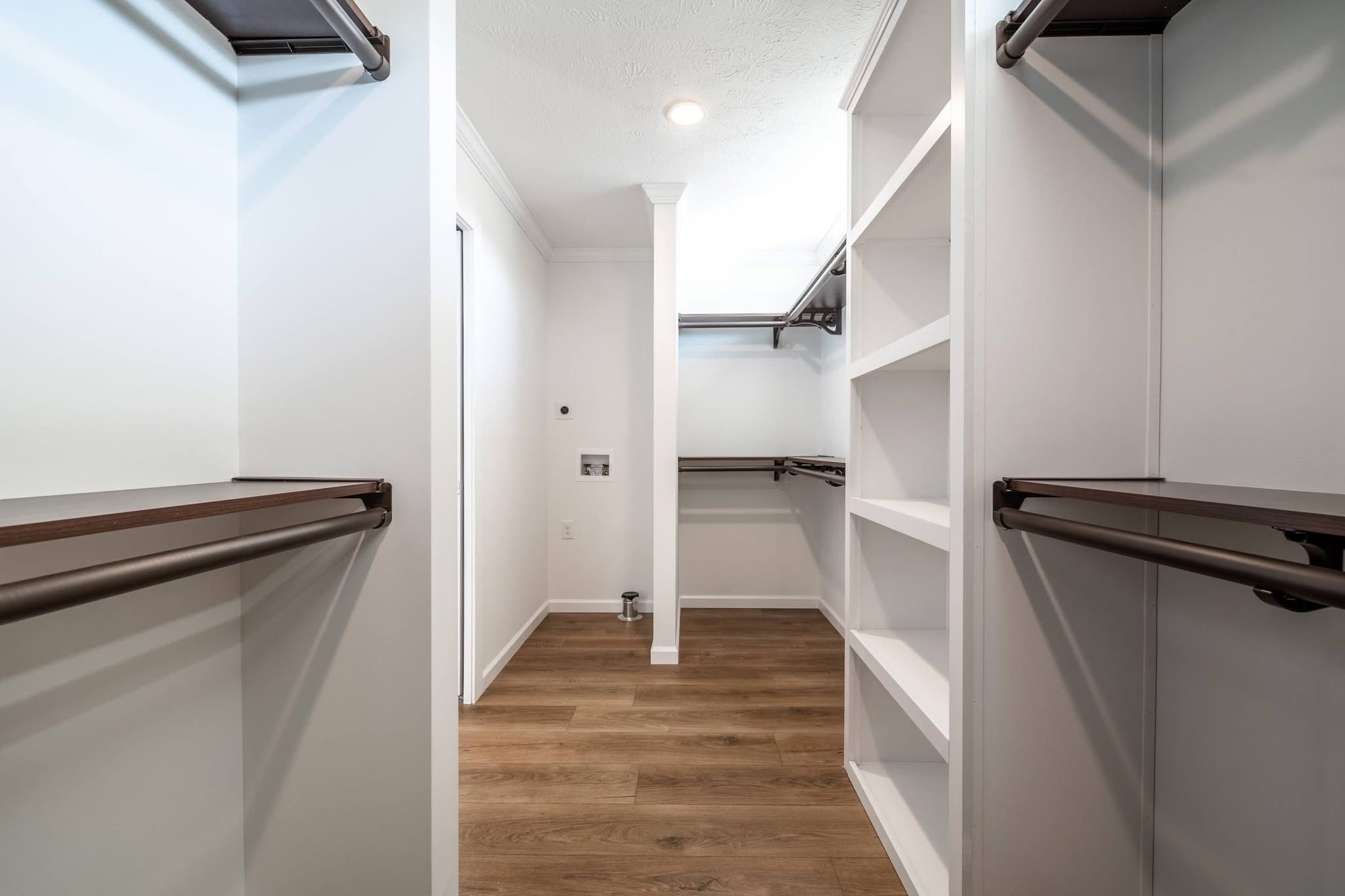 Spacious walk-in closet with wooden floors, white walls, and multiple dark brown shelves and hanging rods. Bright lighting creates a clean, organized feel.