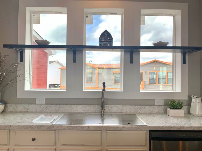 Modern kitchen with marble countertop, stainless steel sink, and faucet. Three windows above with a shelf holding decor, bright and airy ambiance.