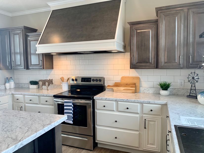 Modern kitchen with a stainless steel stove and black range hood. White subway tiles, marble countertops, gray cabinets, and decor create a clean, cozy feel.