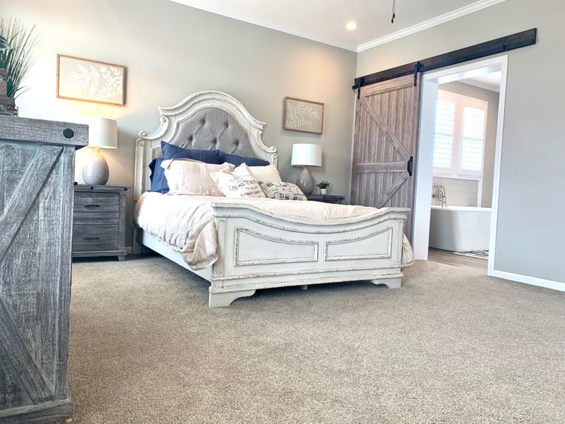 Elegant bedroom with a plush, tufted headboard, light bedding, and dark wooden nightstands. A rustic sliding barn door leads to a bright bathroom.
