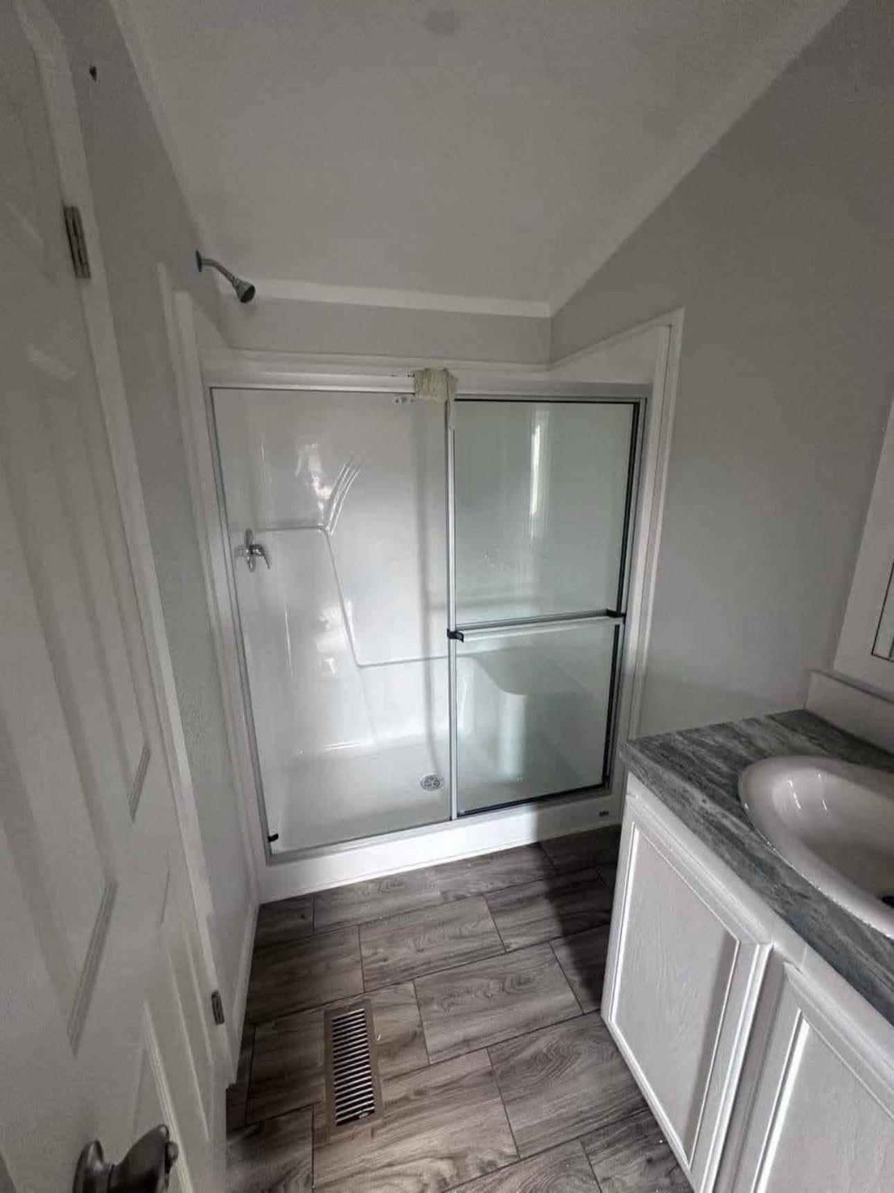 Small bathroom with a glass-enclosed shower, gray tile floor, and white vanity with a granite countertop. The space is bright and modern.