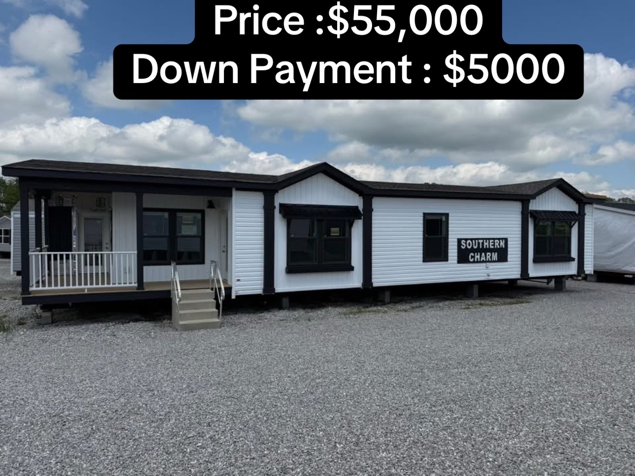 Manufactured home labeled "Southern Charm" with white siding and black trim. Price: $55,000, Down Payment: $5,000. Set on gravel lot under a blue sky.