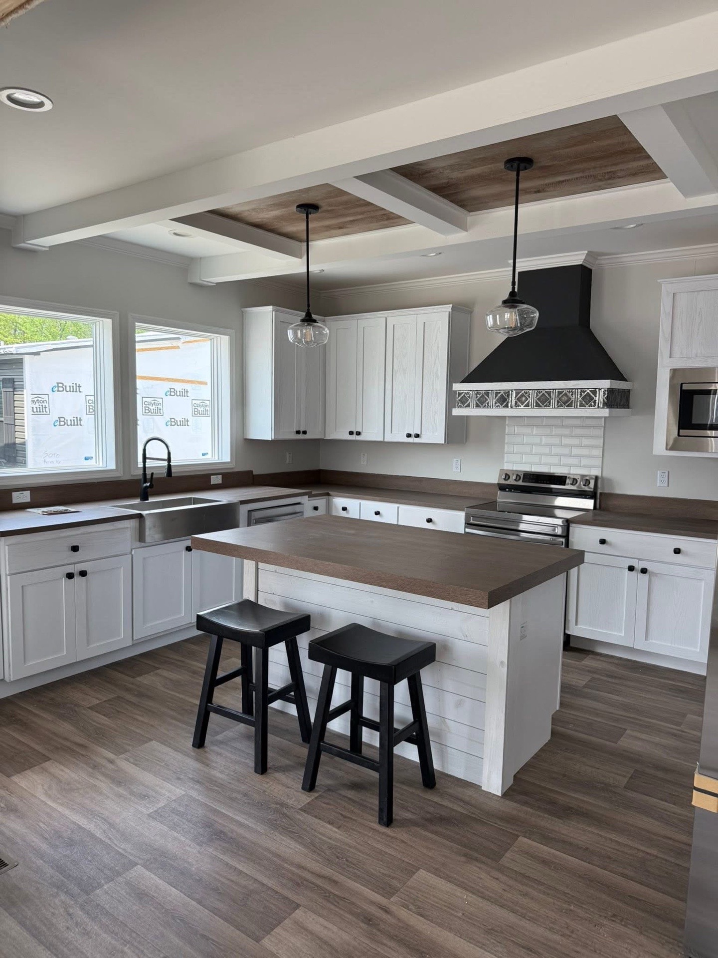 Modern kitchen with white cabinets, a dark wood island, and two black stools. Stainless steel appliances and black range hood add contrast. Bright and spacious.