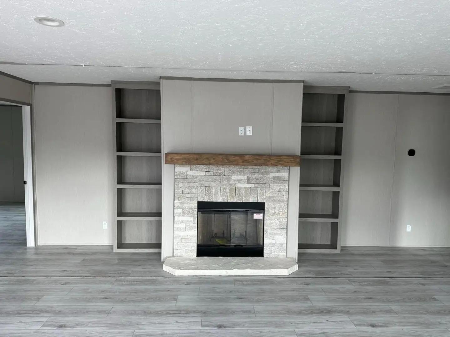 Modern living room with a central stone fireplace, wooden mantel, and built-in shelves on either side. The space has a minimalist and neutral tone.