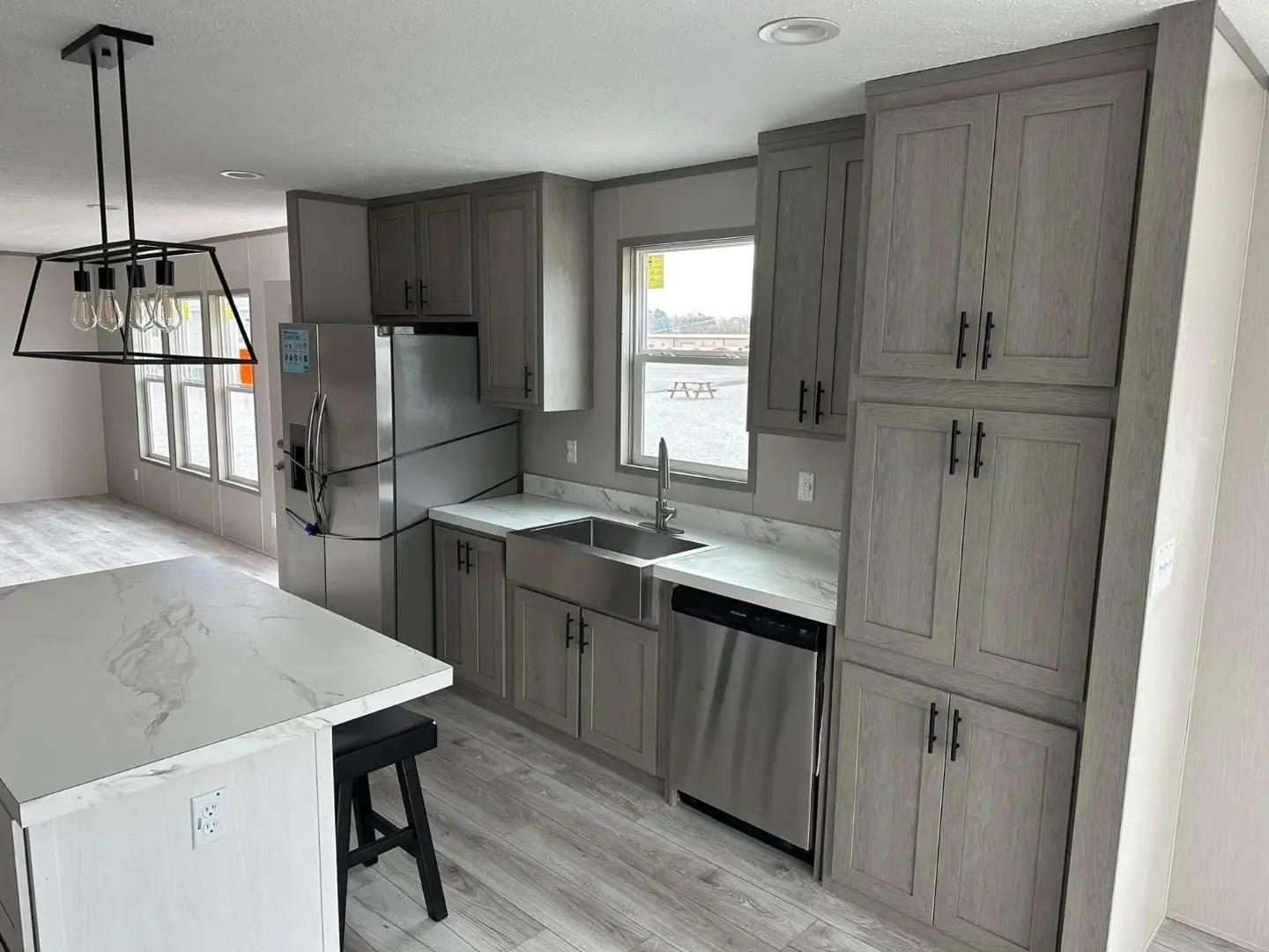 Modern kitchen with gray cabinets, stainless steel appliances, and a large farmhouse sink. Marble island with a black stool and a stylish light fixture.