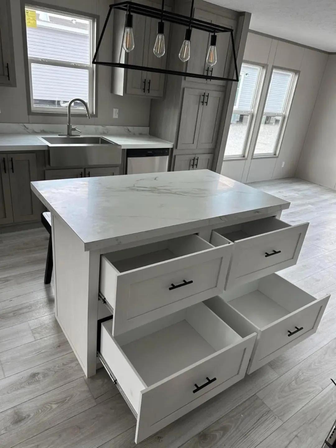 Modern kitchen with light-colored cabinets, an island with four open drawers, and a black pendant light fixture. Bright, spacious, and minimalistic.