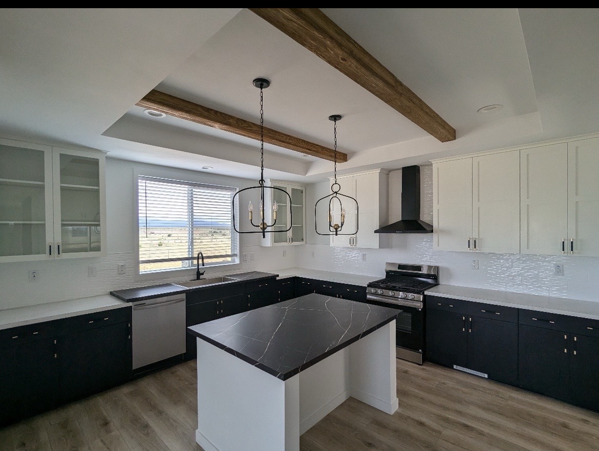Modern kitchen with black and white cabinetry, marble island countertop, stainless steel appliances, wooden ceiling beams, and pendant lights. Bright and spacious.