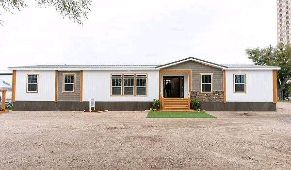 A modern white and gray modular home with a gabled roof and wooden accents. It features a central front porch with steps and minimal landscaping.