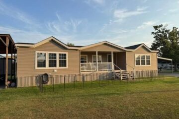 Single-story beige house with white trim, featuring a covered porch and steps, surrounded by a lawn under a blue sky with wispy clouds.