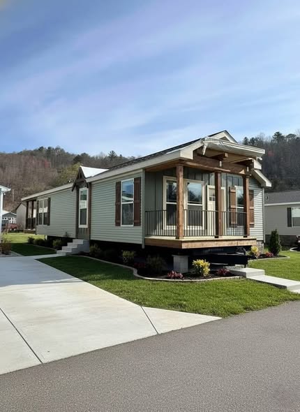 A modern modular home with beige siding, wooden accents, and large windows sits on a green lawn. The sky is clear, adding a serene feel to the suburban scene.