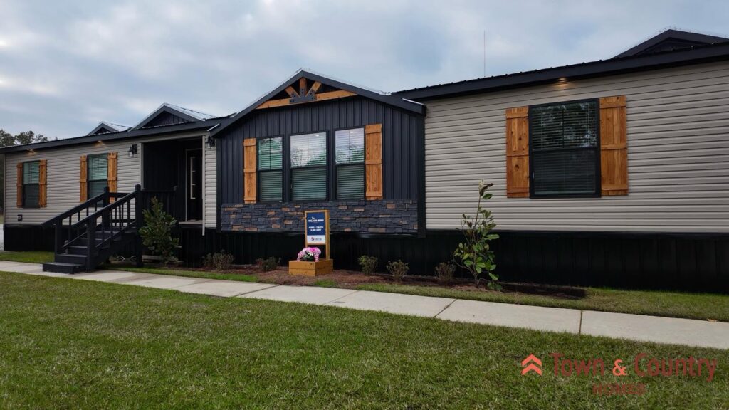 A modern single-story home with dark and light siding, wooden shutters, and a small front garden. The entrance features a black stairway. "Town & Country" logo is visible.