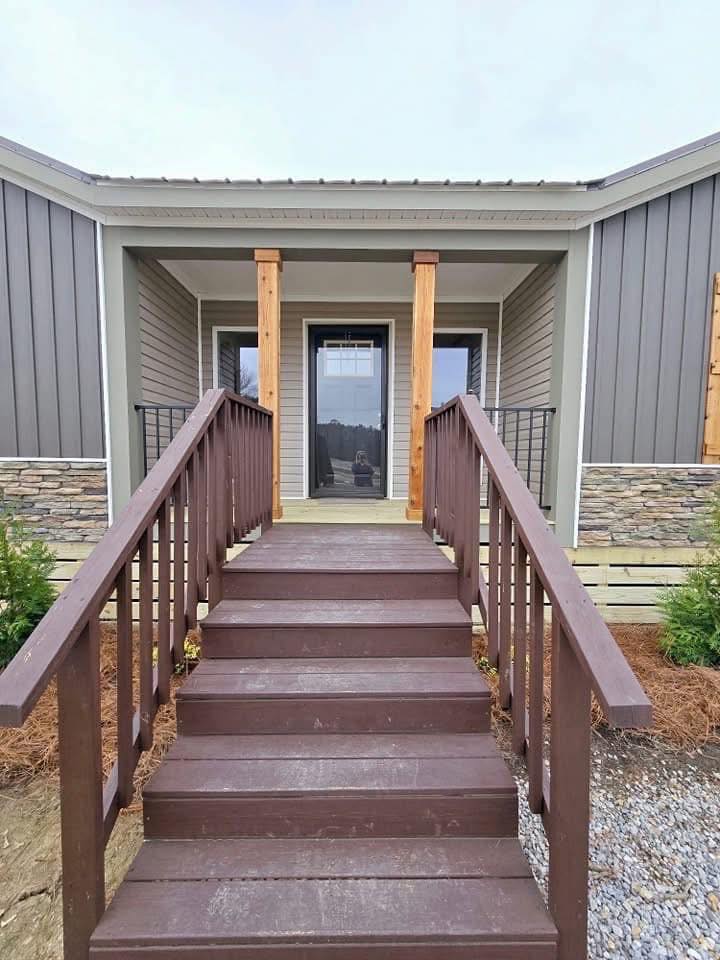 Front entrance of a modern house featuring wooden steps and railings leading to a glass door. The siding combines stone and vertical paneling, creating a warm and inviting look.