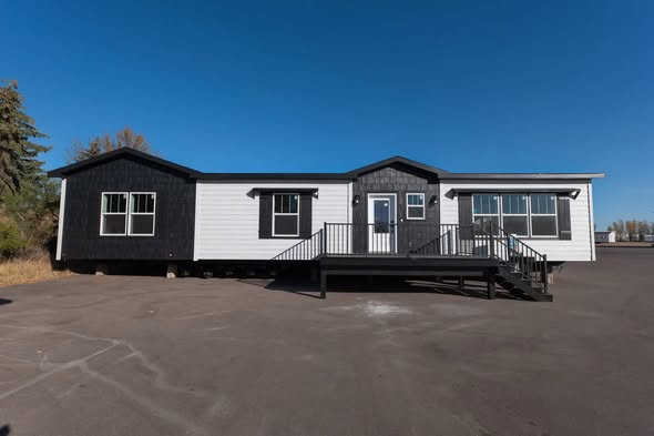 Single-story modular home with black and white siding under a clear blue sky. The front porch has steps leading up, creating a welcoming entrance.