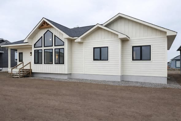 A modern, single-story house with beige siding and dark window frames. The facade features large triangular windows and a small wooden porch.