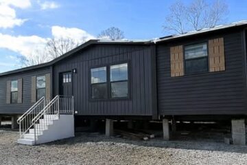 Alt text: "Modern dark gray home with white stairs, featuring three large windows and three sections. Text reads: '3 Bed / 2 Bath 1,568 sqft.' Blue sky overhead."