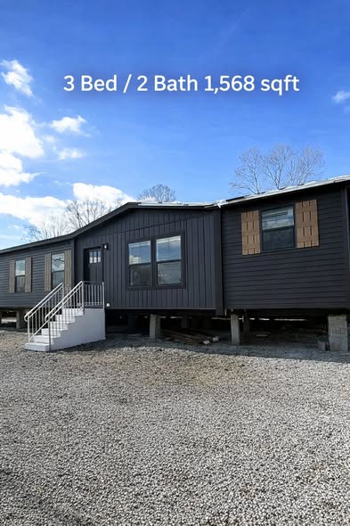 Alt text: "Modern dark gray home with white stairs, featuring three large windows and three sections. Text reads: '3 Bed / 2 Bath 1,568 sqft.' Blue sky overhead."