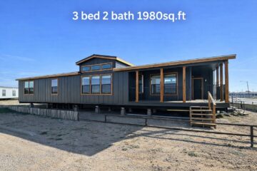 Modern grey modular home with wooden accents, elevated on a lot with a porch. Text reads "3 bed 2 bath 1980 sq. ft." under a clear blue sky.