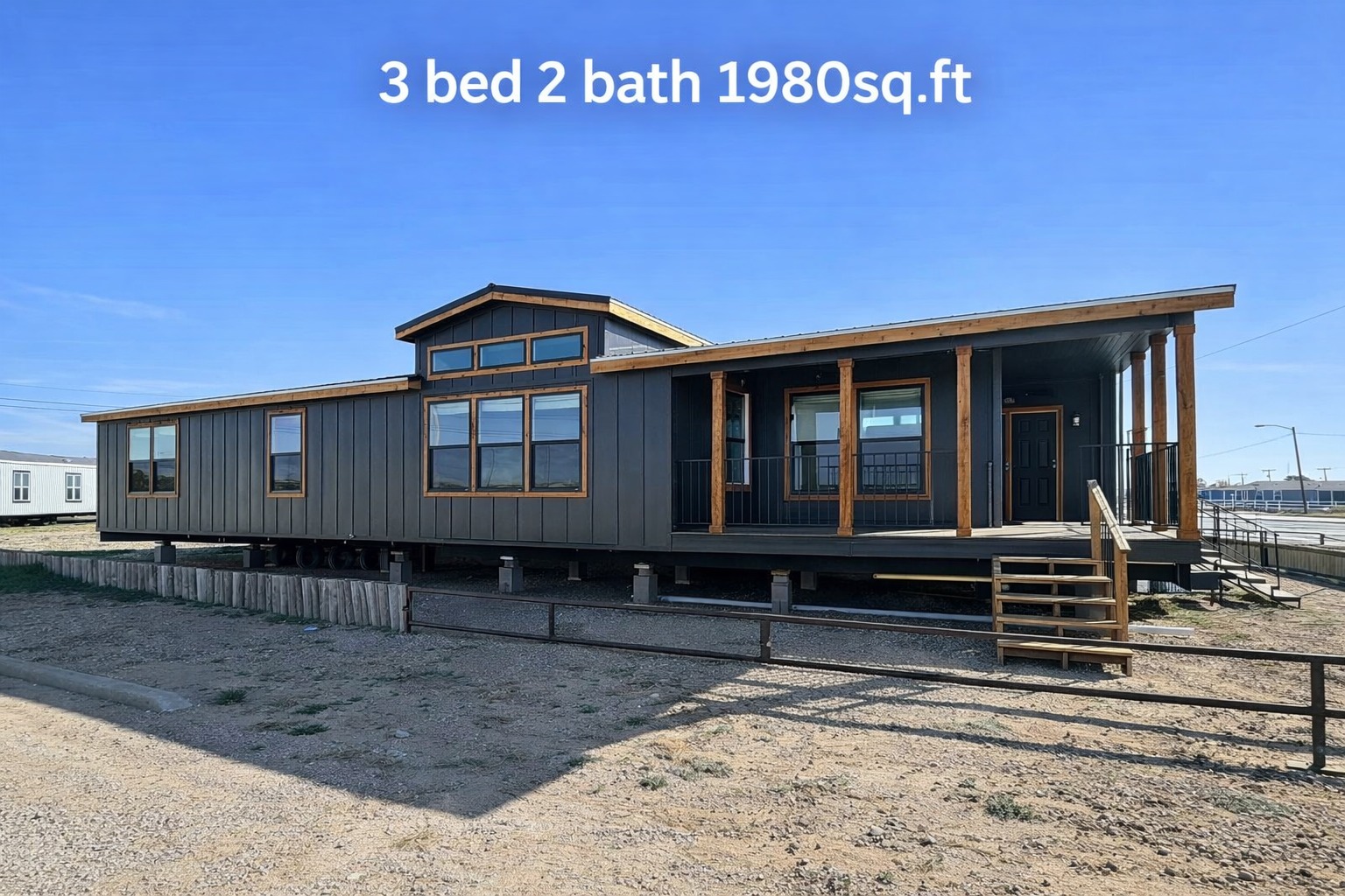 Modern grey modular home with wooden accents, elevated on a lot with a porch. Text reads "3 bed 2 bath 1980 sq. ft." under a clear blue sky.