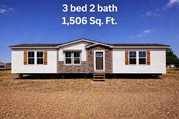 A modern manufactured home with white siding and stone accents is set on a dirt lot under a clear blue sky. Text reads "3 bed 2 bath, 1,506 Sq. Ft."