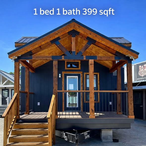 Compact tiny house with blue siding and natural wood accents, front porch, and stairs. Text reads "1 bed 1 bath 399 sqft" against a clear sky.