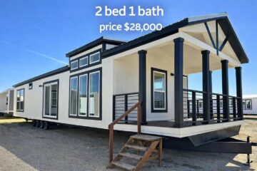 Modern white mobile home with black trim, front porch, and large windows. Text reads "2 bed 1 bath, price $28,000." Bright, clear day.