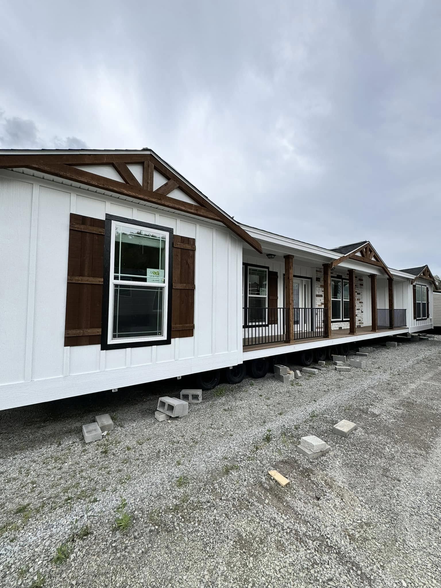 Modular home with white siding and wooden trim, elevated on concrete blocks, under a cloudy sky. The house features large windows and a small porch.