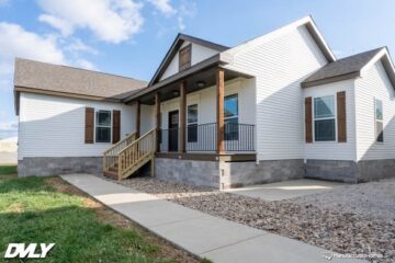 A modern white house with a gabled roof, front porch, wooden shutters, and stone foundation. A sidewalk leads to the steps. Bright, sunny day.