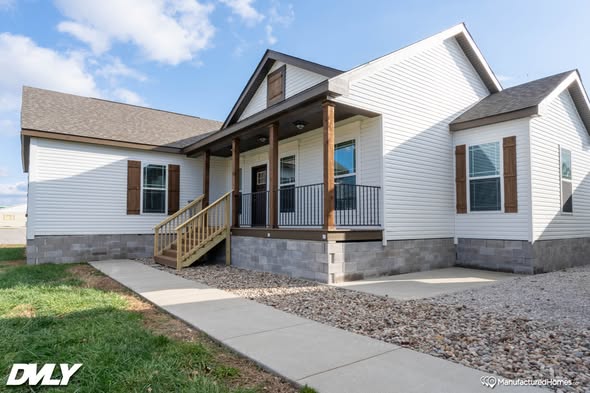 A modern white house with a gabled roof, front porch, wooden shutters, and stone foundation. A sidewalk leads to the steps. Bright, sunny day.