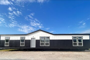 A modern, black and white modular home with large windows under a bright blue sky. The design is sleek and contemporary, evoking a sense of simplicity.