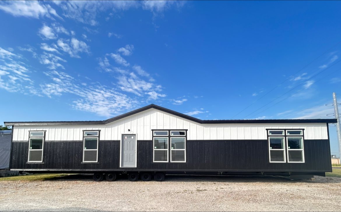 A modern, black and white modular home with large windows under a bright blue sky. The design is sleek and contemporary, evoking a sense of simplicity.