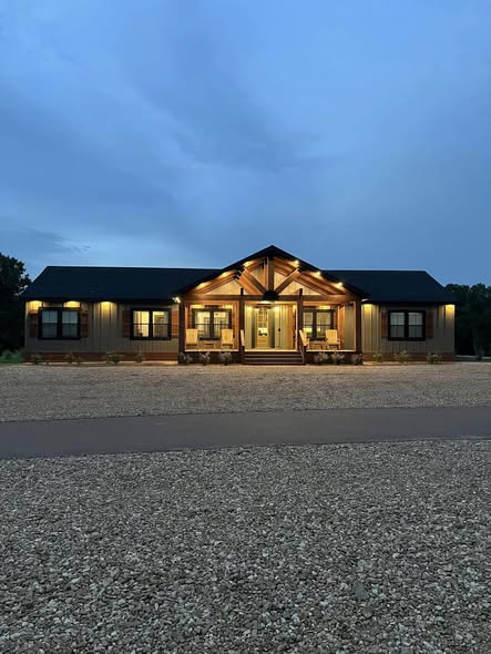 Single-story house at dusk, softly lit with warm lights. It has a gabled roof, large porch, and stone pathway, creating a welcoming, serene atmosphere.