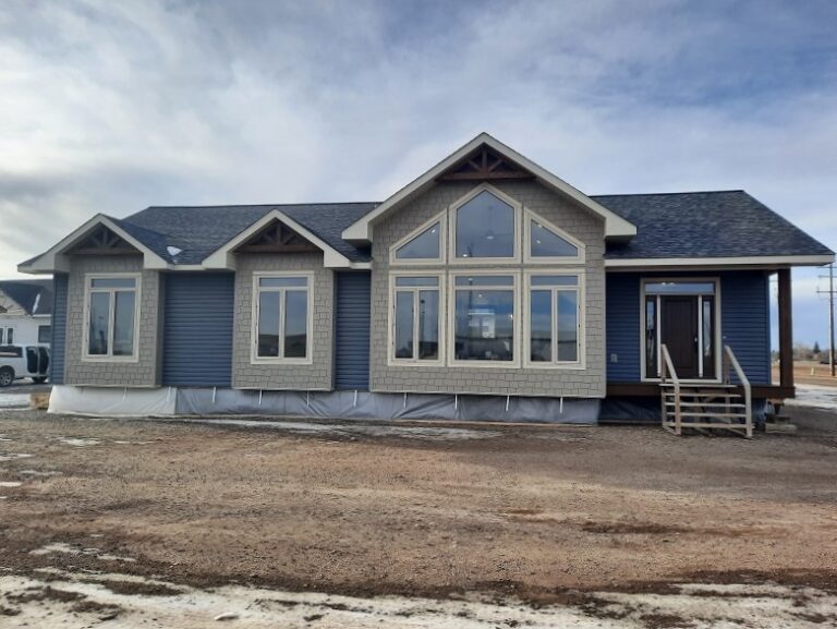 Single-story house with blue siding and large front windows, under a cloudy sky. Rustic, welcoming design with a small porch and steps.
