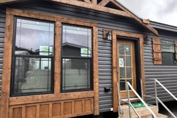 Cozy cabin with dark siding and wooden accents under a cloudy sky. Features large windows, a front door with the number 3, and stair access.